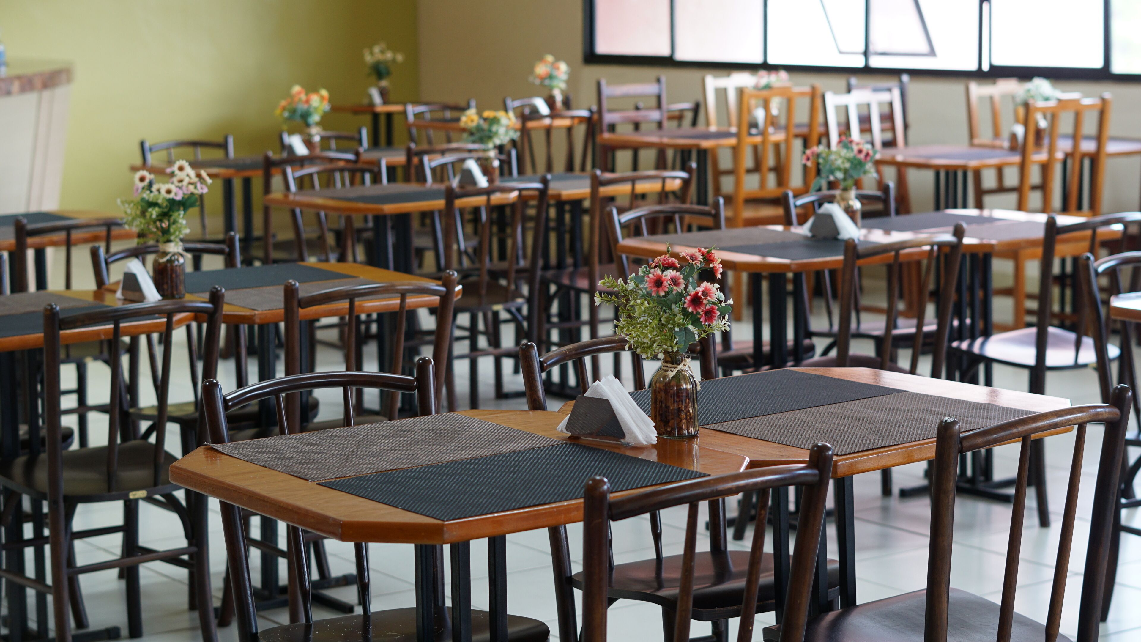 Un restaurante con varias mesas y sillas de madera, algunas con centros de mesa florales.