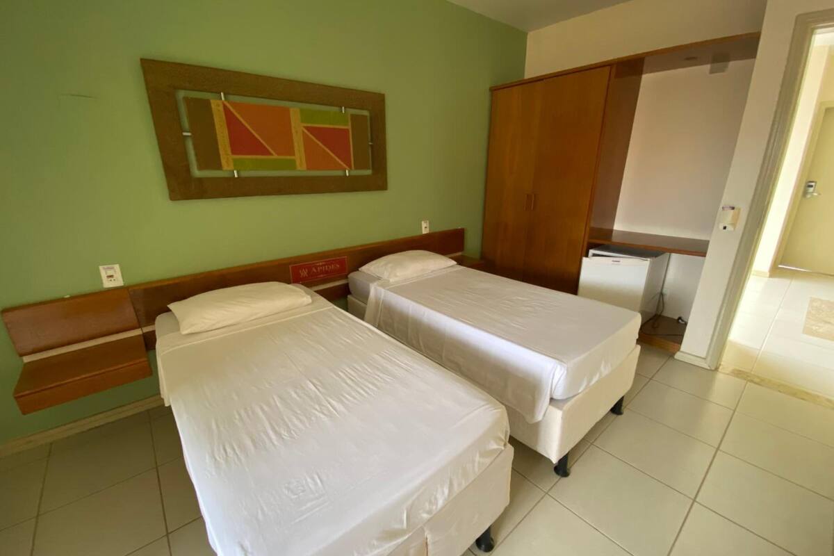 Ein Hotelzimmer mit zwei Betten, einem Holzschrank, einem kleinen Schreibtisch und einem an der Wand hängenden Kunstwerk.