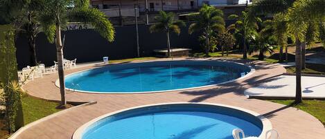 Une piscine divisée en deux zones distinctes, entourée de palmiers et bordée d’une terrasse dallée.