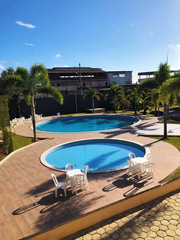 A swimming pool with two separate sections, surrounded by palm trees and a paved deck.