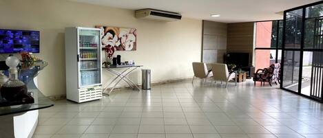 A modern hotel lobby with a large glass door, a refrigerator stocked with beverages, a flat-screen TV, and a decorative orchid.
