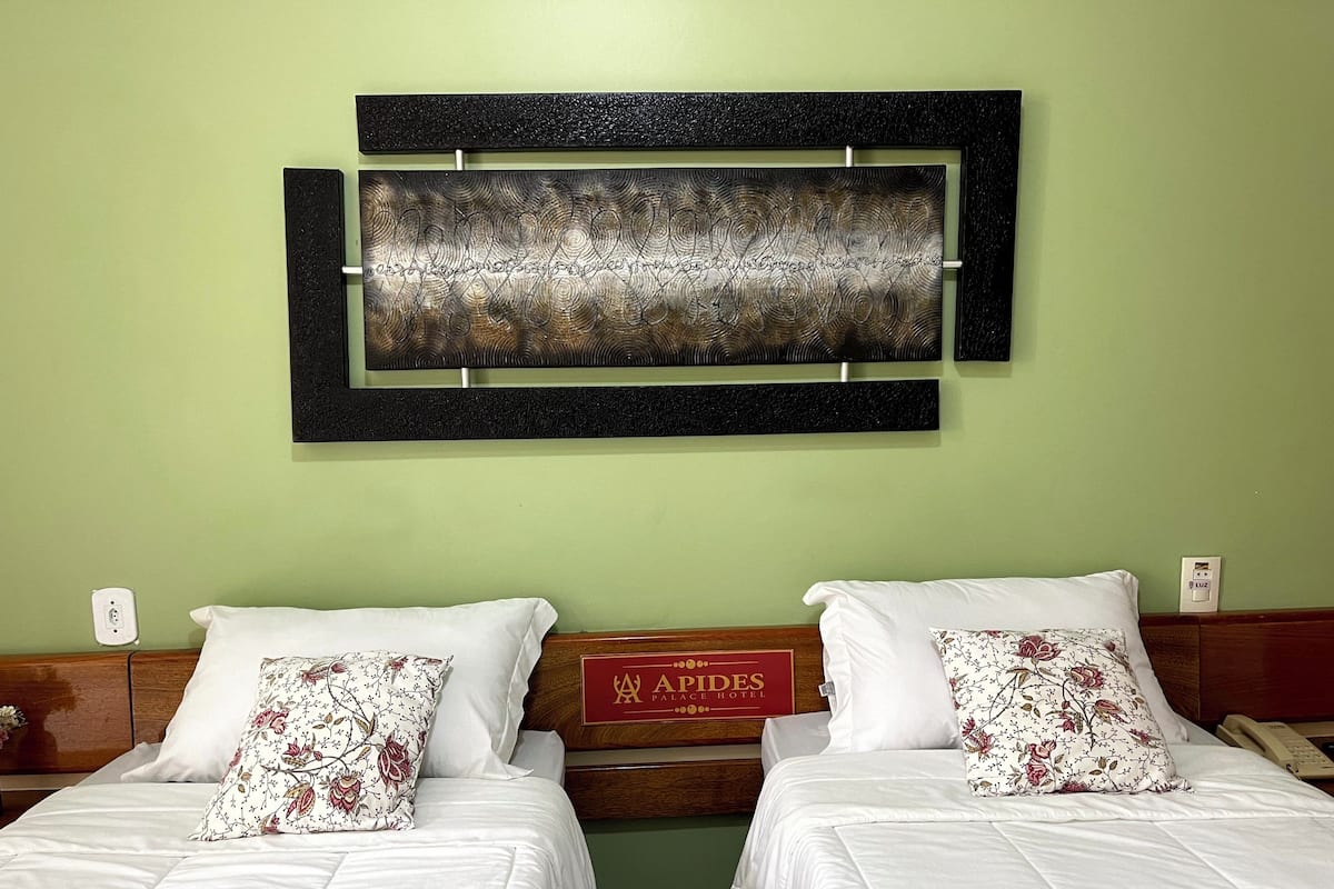 Ein Hotelzimmer mit zwei Betten, jeweils mit weißer Bettwäsche und Kissen mit Blumenmuster. Darüber befindet sich ein großes abstraktes Kunstwerk.
