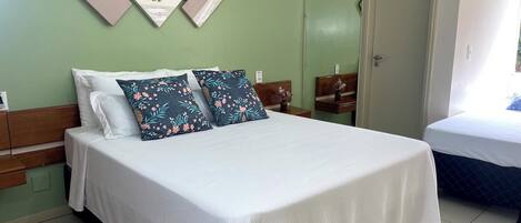A neatly made bed with white bedding and two floral pillows, a wooden headboard, and a green wall with three framed pictures.