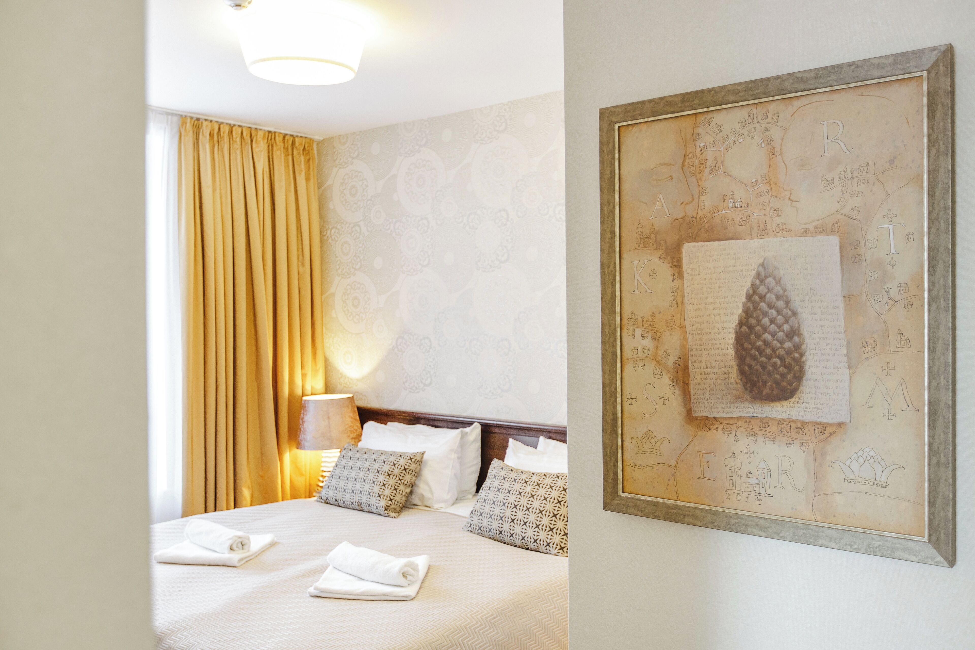 A hotel room with a neatly made bed, a lamp, and a framed map on the wall.