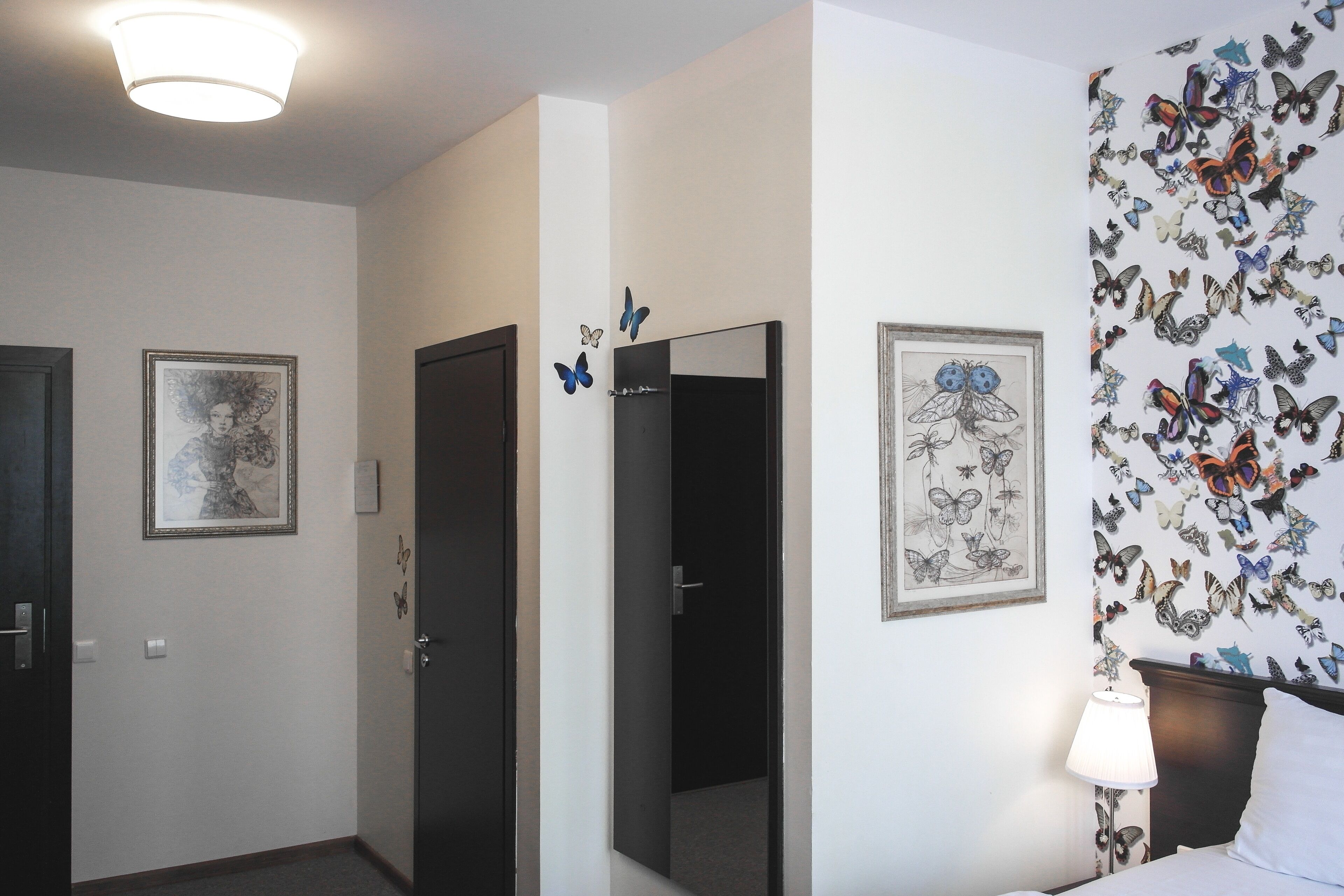 Habitación de hotel con cama, mesita de noche, lámpara y decoración de mariposas en la pared.