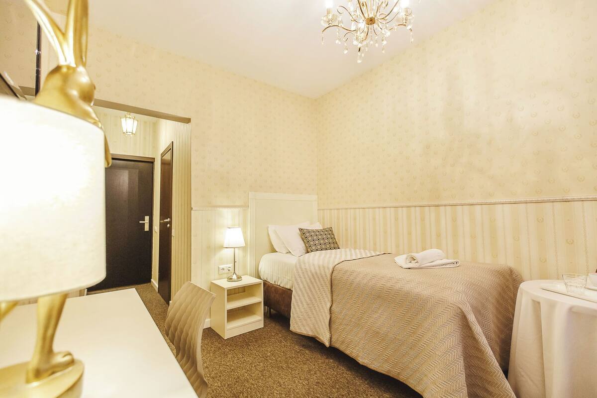 A hotel room with a bed, bedside table, lamp, and a chandelier.