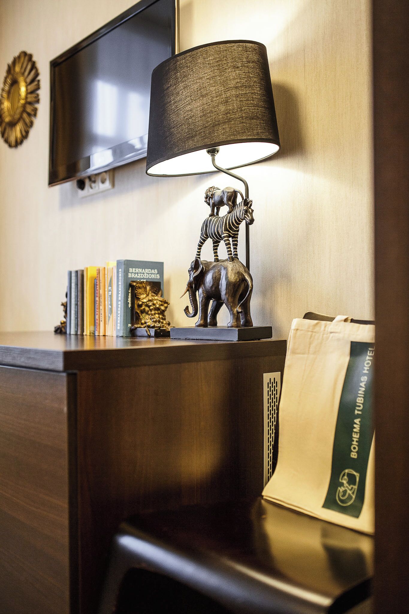 A hotel desk with a lamp, a television, books, a zebra statue, and a guest bag.