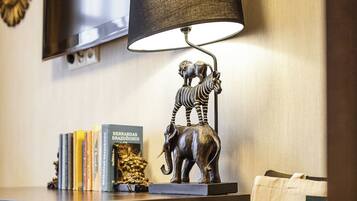 A hotel desk with a lamp, a television, books, a zebra statue, and a guest bag.