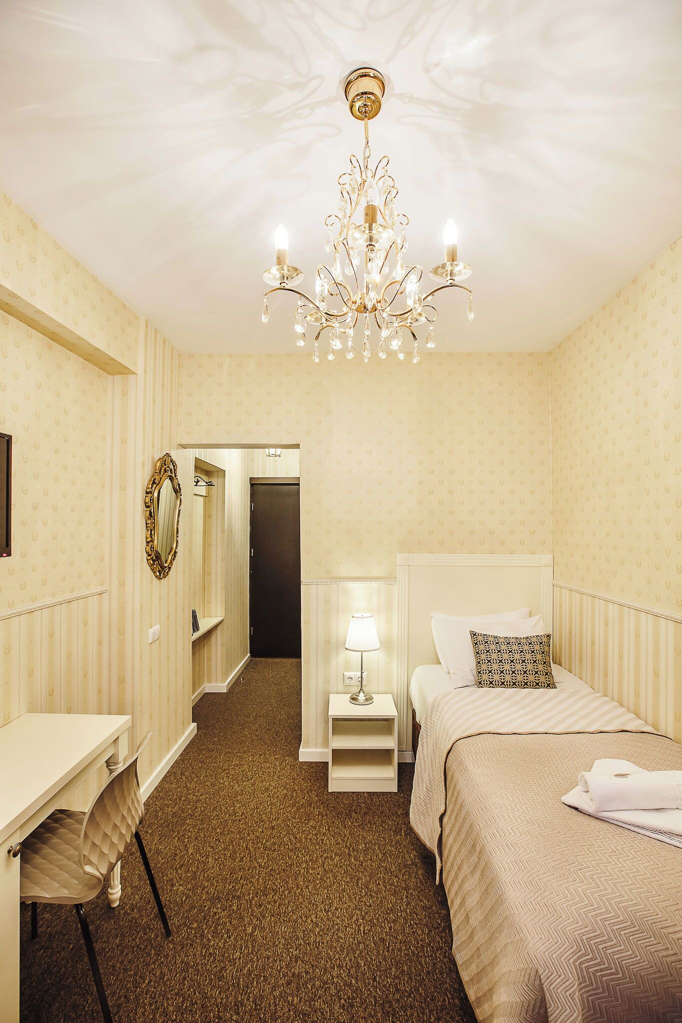 A hotel room with a bed, bedside table, lamp, and a mirror on the wall.