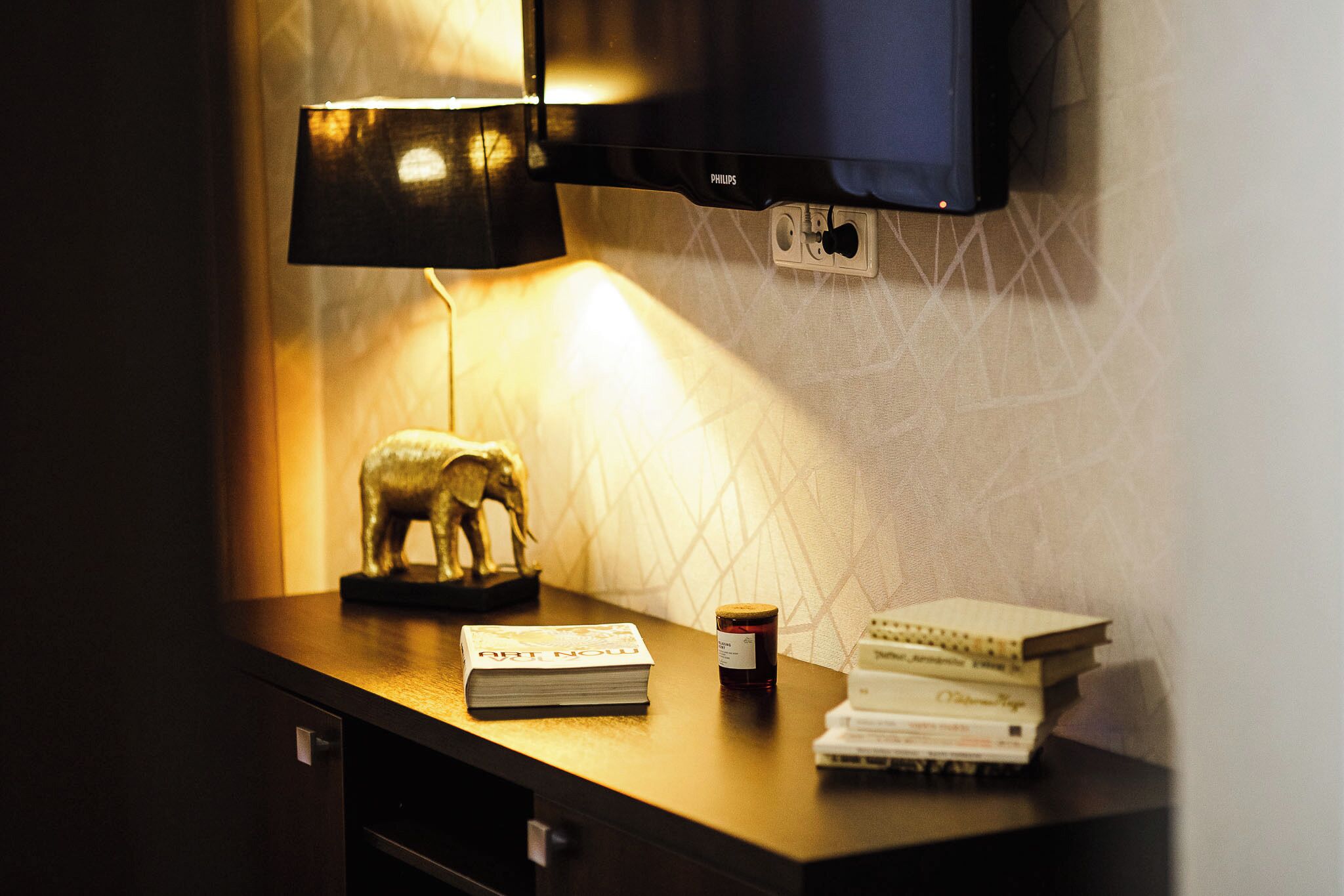 A desk with a lamp, a book, a bottle, and a television.