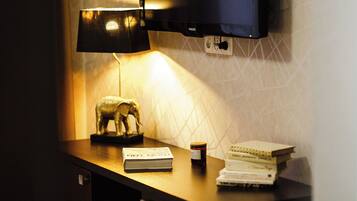 A desk with a lamp, a book, a bottle, and a television.