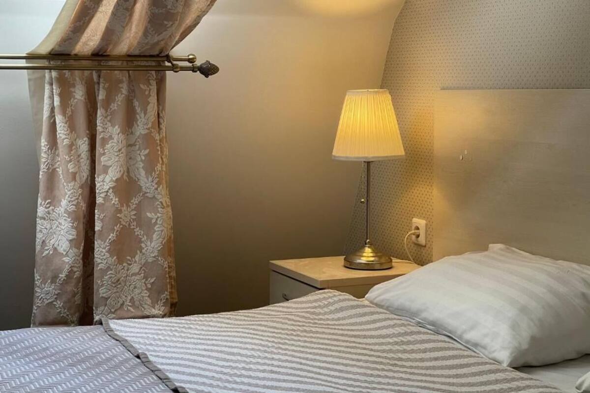 A hotel room with a bed, a nightstand with a lamp, and a window with curtains.