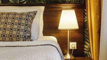 A neatly made bed with patterned pillows, a bedside lamp, and a wall with a leafy pattern.