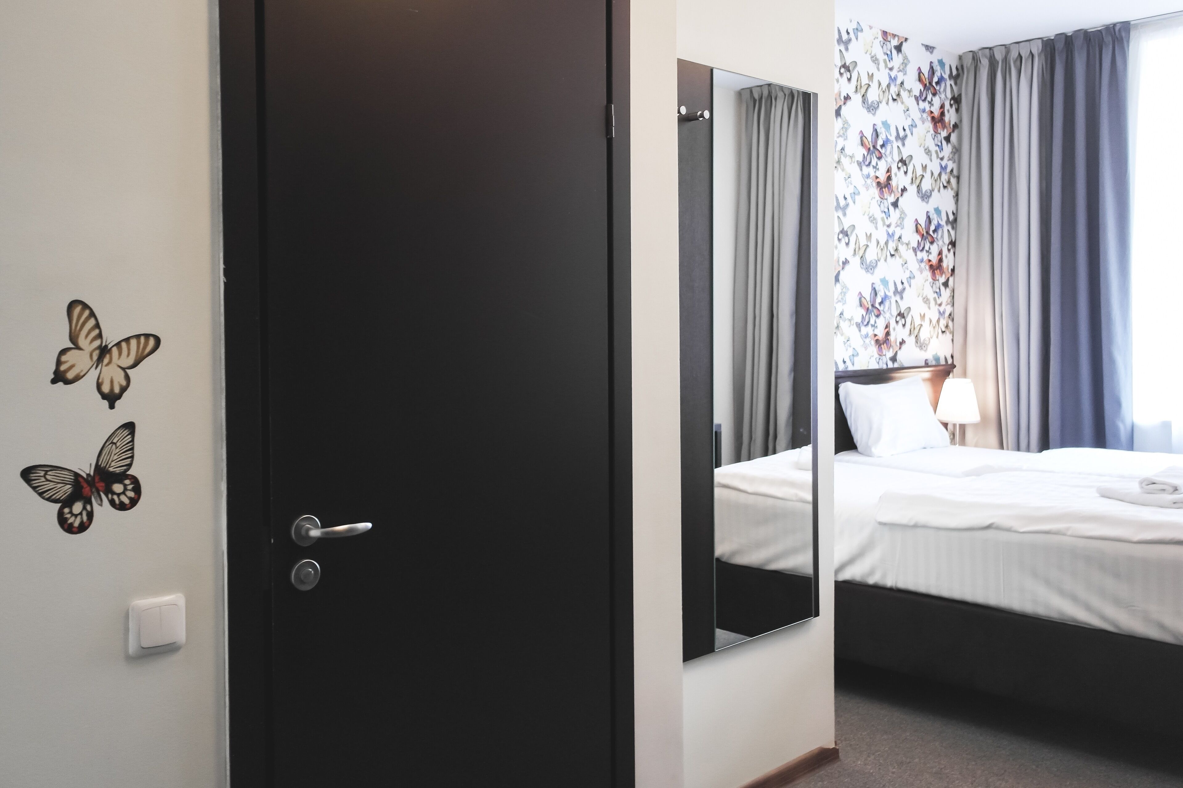 A hotel room with a bed, a mirror, a door, and butterfly decals on the wall.