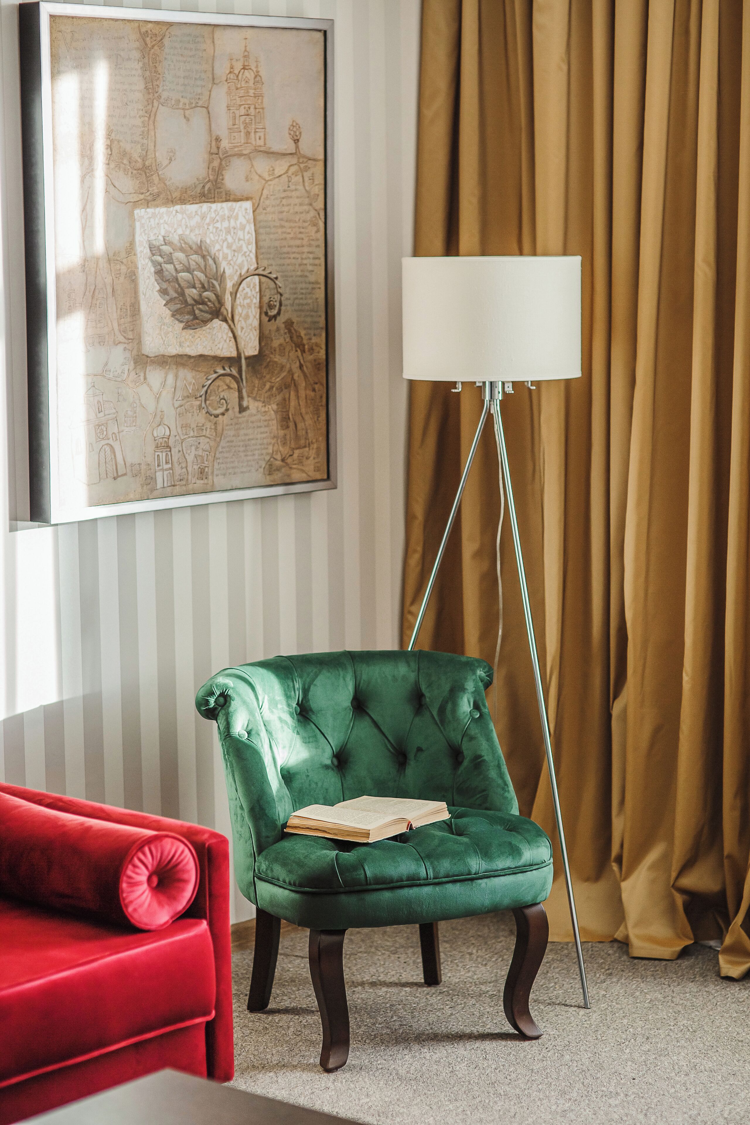 Una habitación con un sillón verde de terciopelo, un sofá rojo, una lámpara de pie y un mapa enmarcado en la pared.