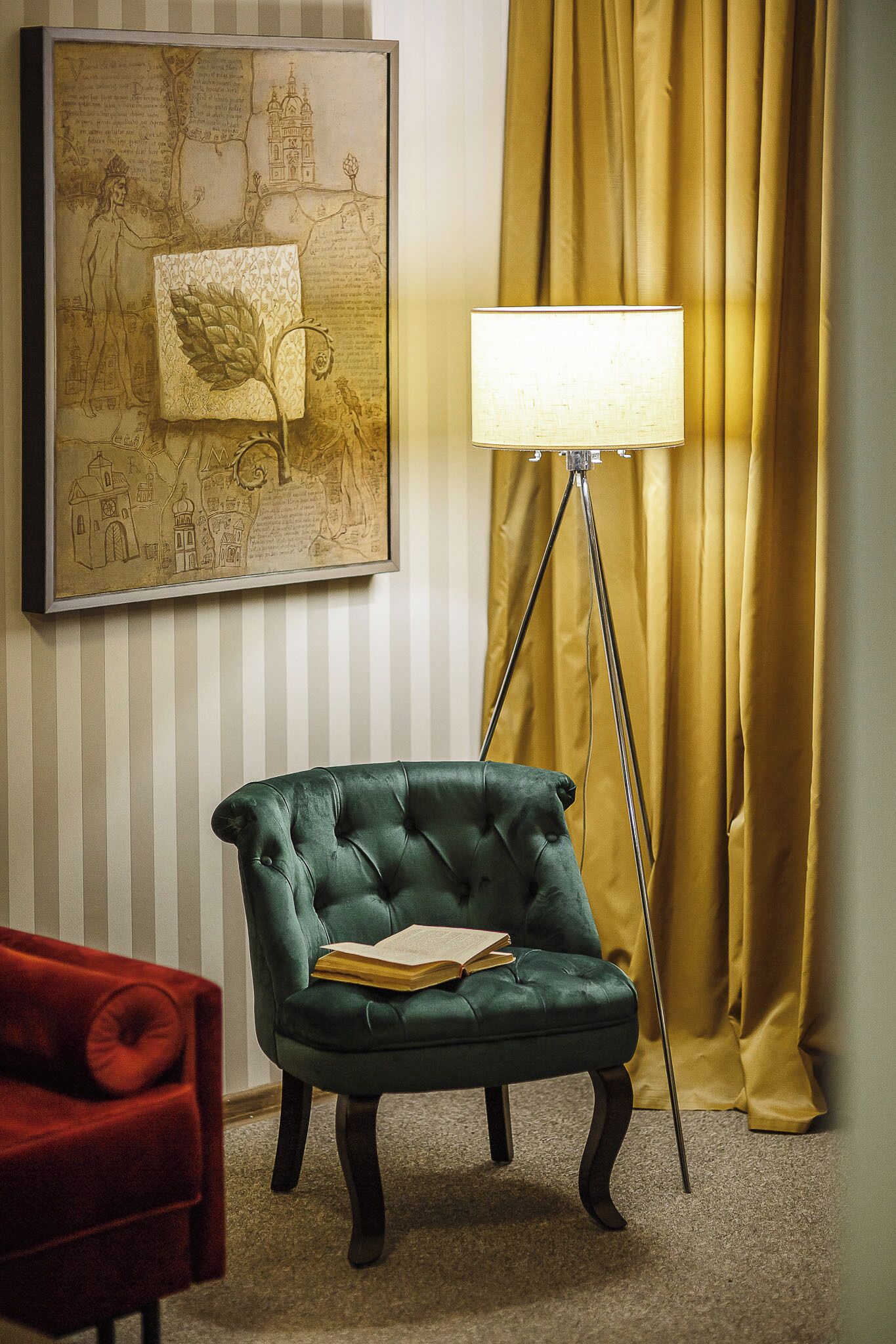 Un fauteuil vert, un livre, une lampe sur pied et une carte encadrée accrochée au mur.