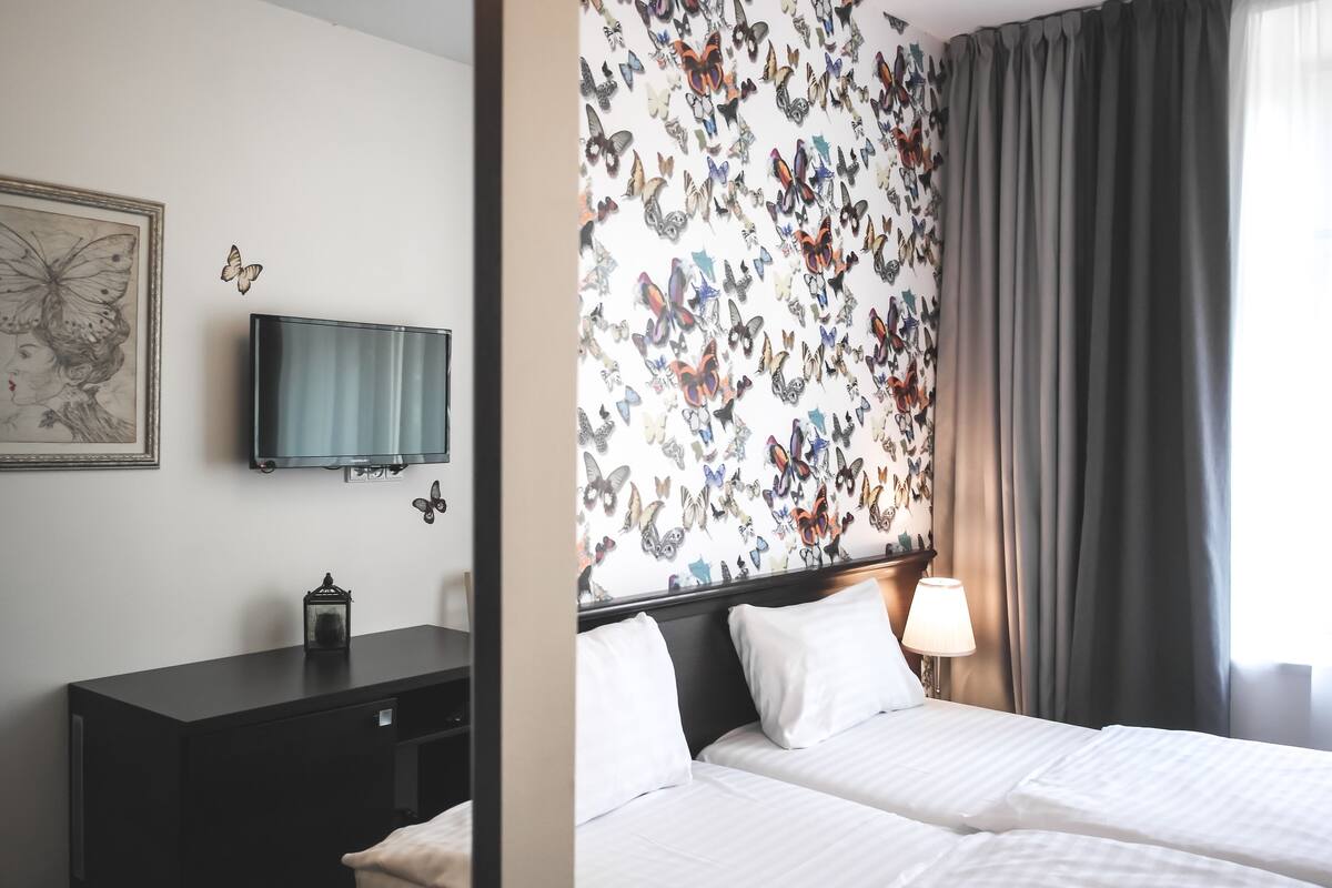 A hotel room with a bed, a TV, a dresser, and a wall with butterfly decals.