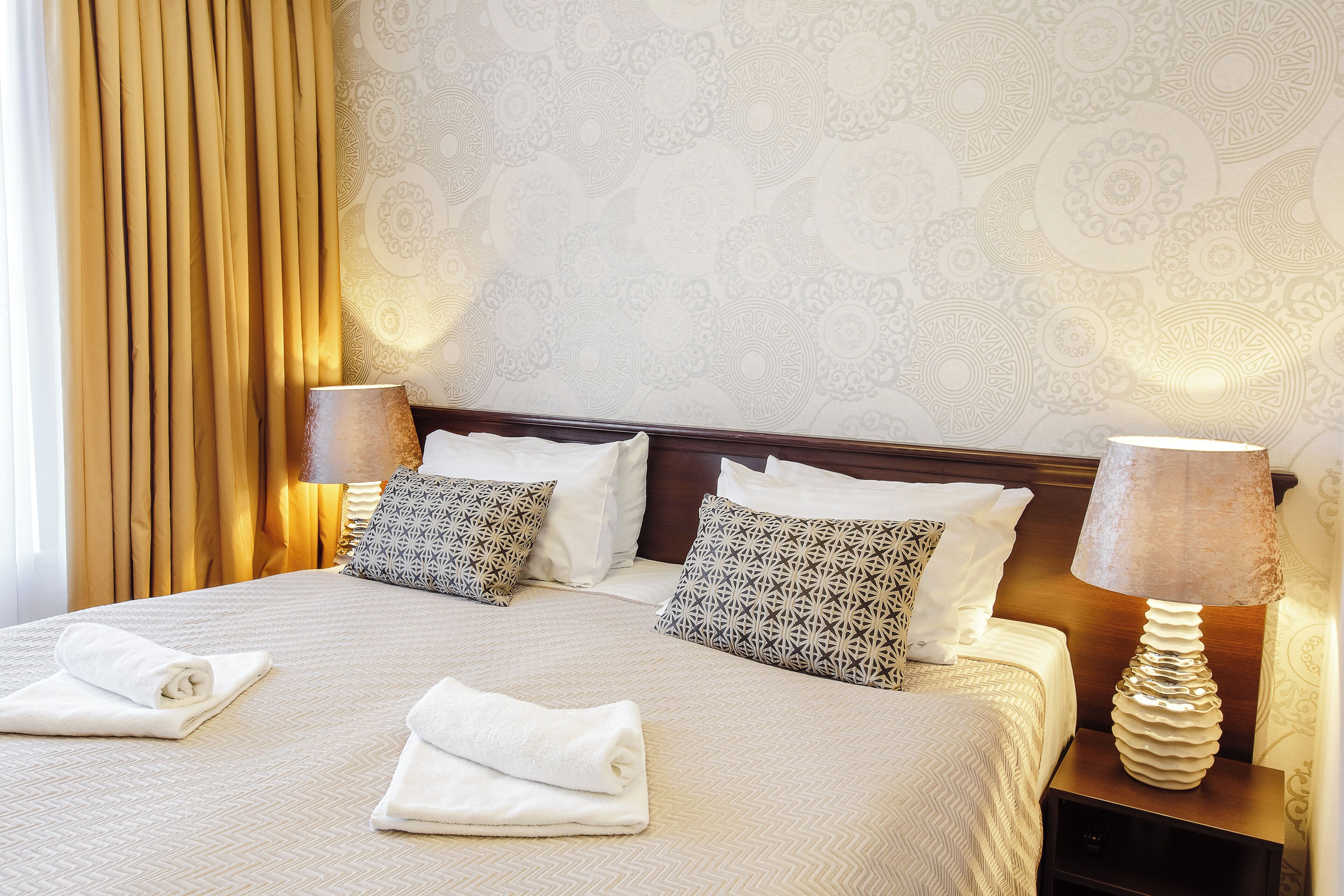 A neatly made bed with two pillows, a bedside lamp, and a folded towel on a hotel room bed.