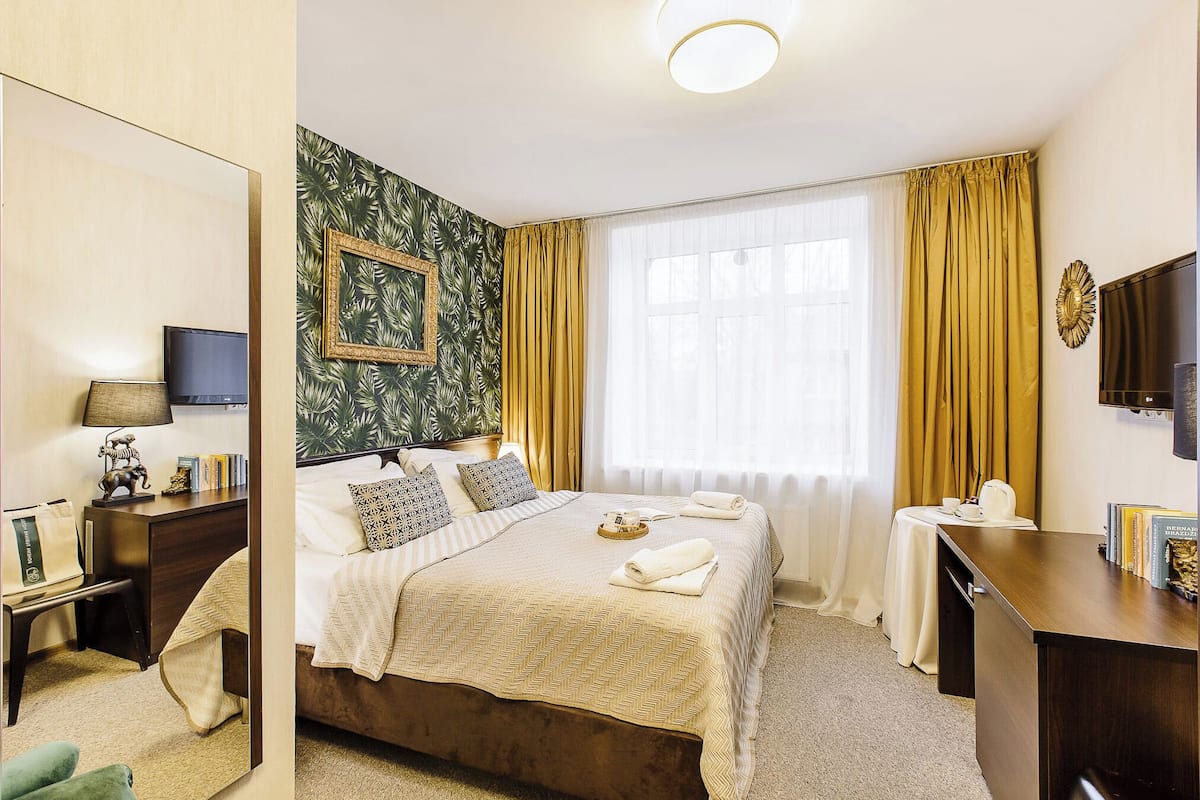 A hotel room with a bed, bedside table, lamp, and a mirror.