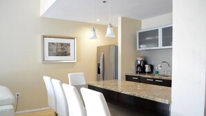 A modern kitchen with a granite countertop, white chairs, a refrigerator, a coffee maker, and a microwave.