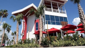 A modern building with a prominent red sign, surrounded by palm trees and red umbrellas.