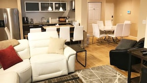 A modern living room with a white sofa, a black armchair, and a dining area with white chairs.