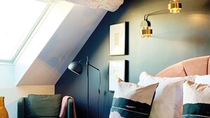 A bedroom with a sloped ceiling, a skylight, a bed with multiple pillows, a chair, and a floor lamp. - Le Globe (Meursault)