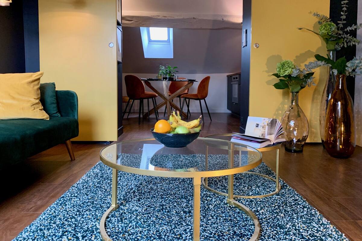 A modern living room with a glass coffee table, a sofa, a dining area with chairs, and a kitchen in the background.