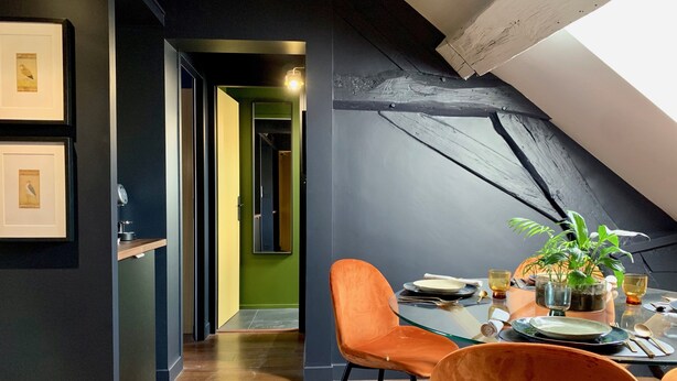 A dining area with a high ceiling, a skylight, and a view of a green room. - Le Globe (Meursault)