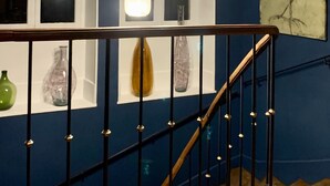 A staircase with a black railing, a blue wall, and a window with multiple hanging lights. - Le Globe (Meursault)
