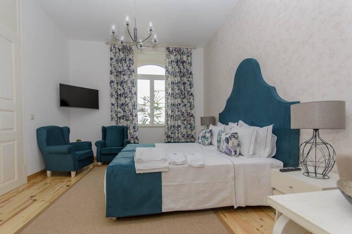 Ein Hotelzimmer mit einem Bett, zwei Sesseln, einem Fernseher, einer Chandelier und einem Vorhangfenster.