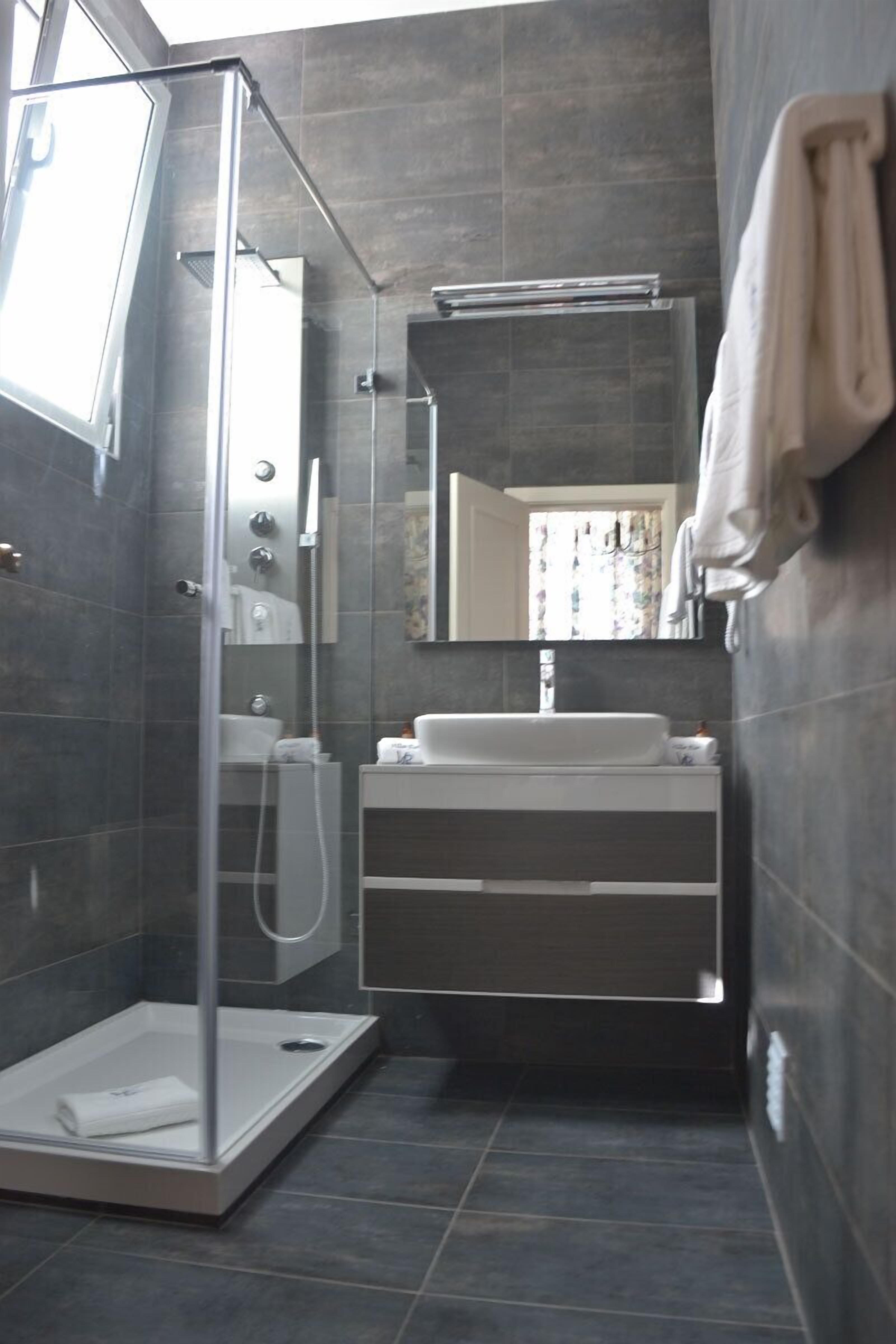 Un baño moderno con cabina de ducha de vidrio, un lavabo blanco y un espejo grande.