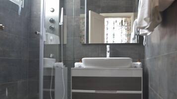 Un baño moderno con cabina de ducha de vidrio, un lavabo blanco y un espejo grande.