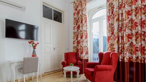 A living room with a flat-screen TV, a grey chair, a red armchair, and a small table with a vase of flowers. - Villa Rio Guest House Suites (Portimão)