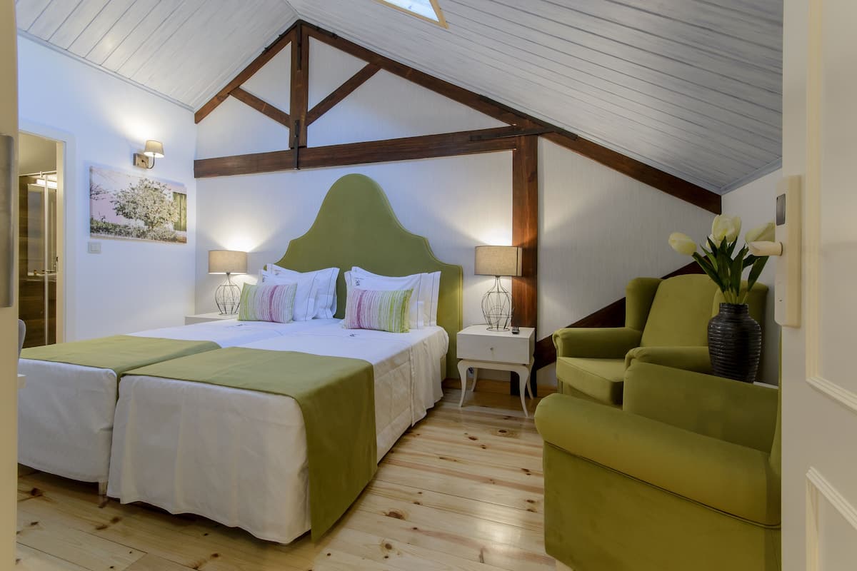 Ein Schlafzimmer mit einem großen Bett, zwei Nachttischen, einem grünen Sessel und einer Blumenvase.