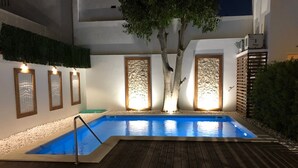 A swimming pool with a wooden deck, surrounded by walls with framed artwork and a tree. - Villa Rio Guest House Suites (Portimão)