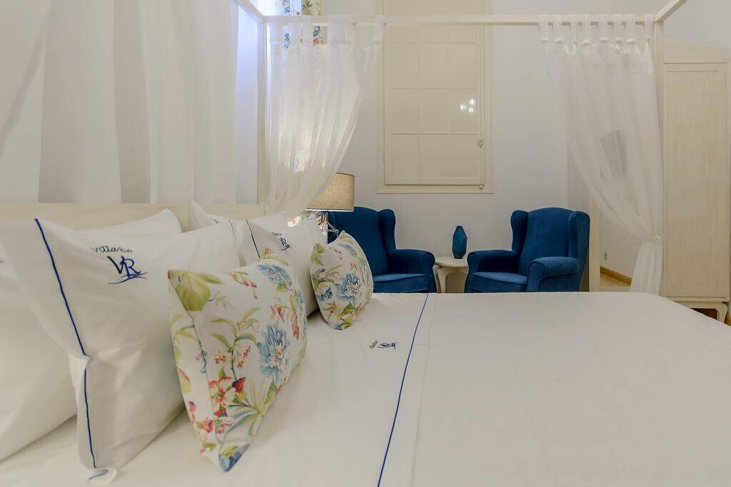 Une chambre à coucher avec un lit, deux chaises bleues, une petite table et une fenêtre avec des rideaux.