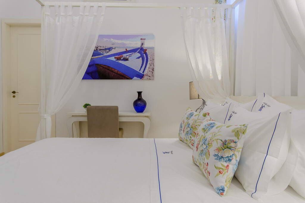 A hotel room with a bed, a desk, a chair, a vase, and a painting on the wall.