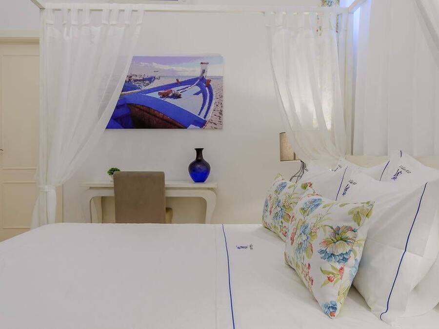 A hotel room with a bed, a desk, a chair, a vase, and a painting on the wall.
