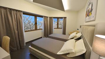 A hotel room with two beds, a chair, a lamp, and large windows with curtains.