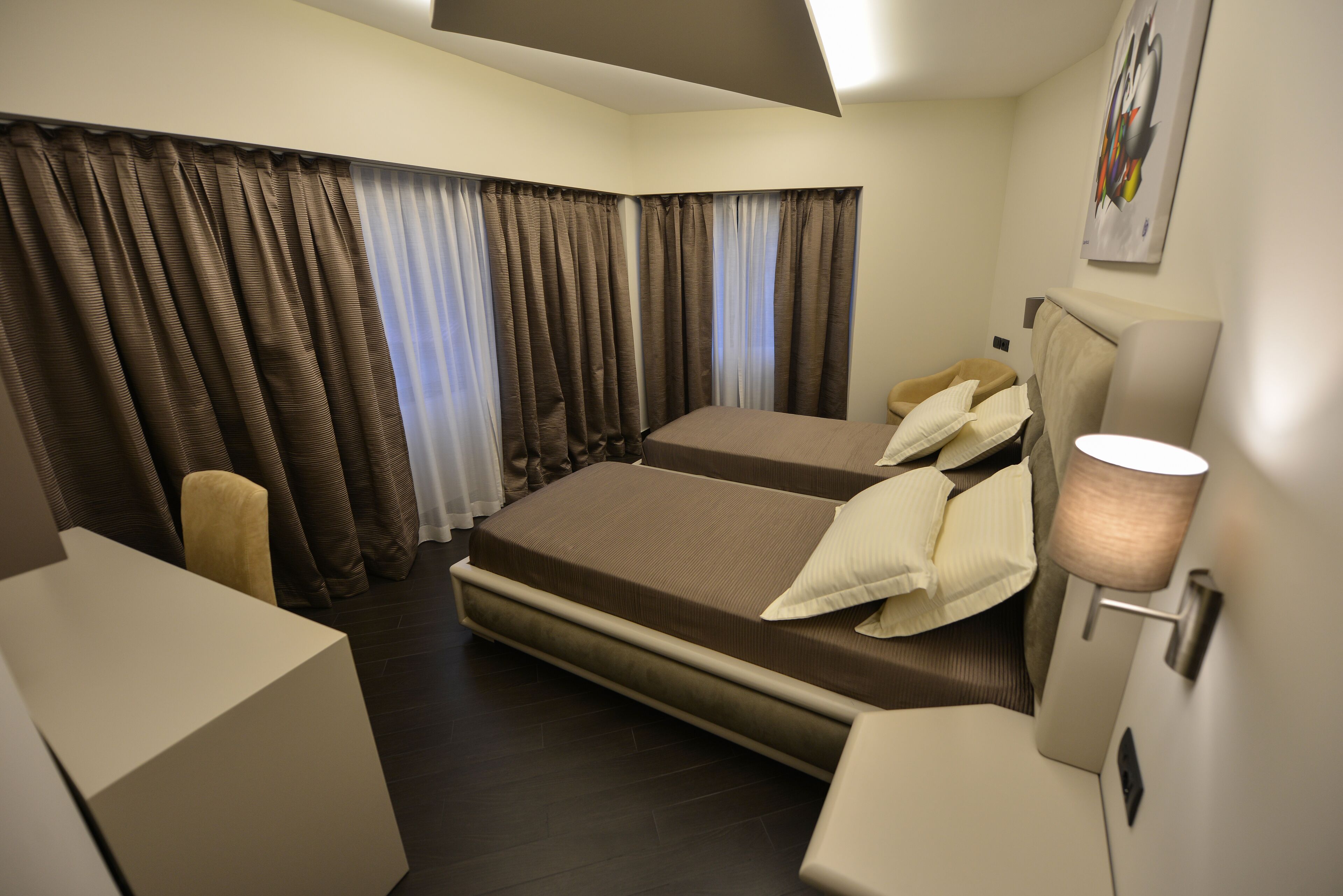 A hotel room with two beds, a desk, a chair, and a lamp.