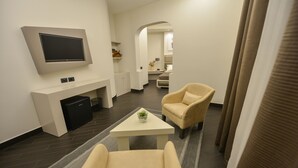 Una sala de estar moderna con un televisor de pantalla plana montado en la pared, un sillón color beige, una pequeña mesa de centro blanca con una planta y un piso de madera oscura.