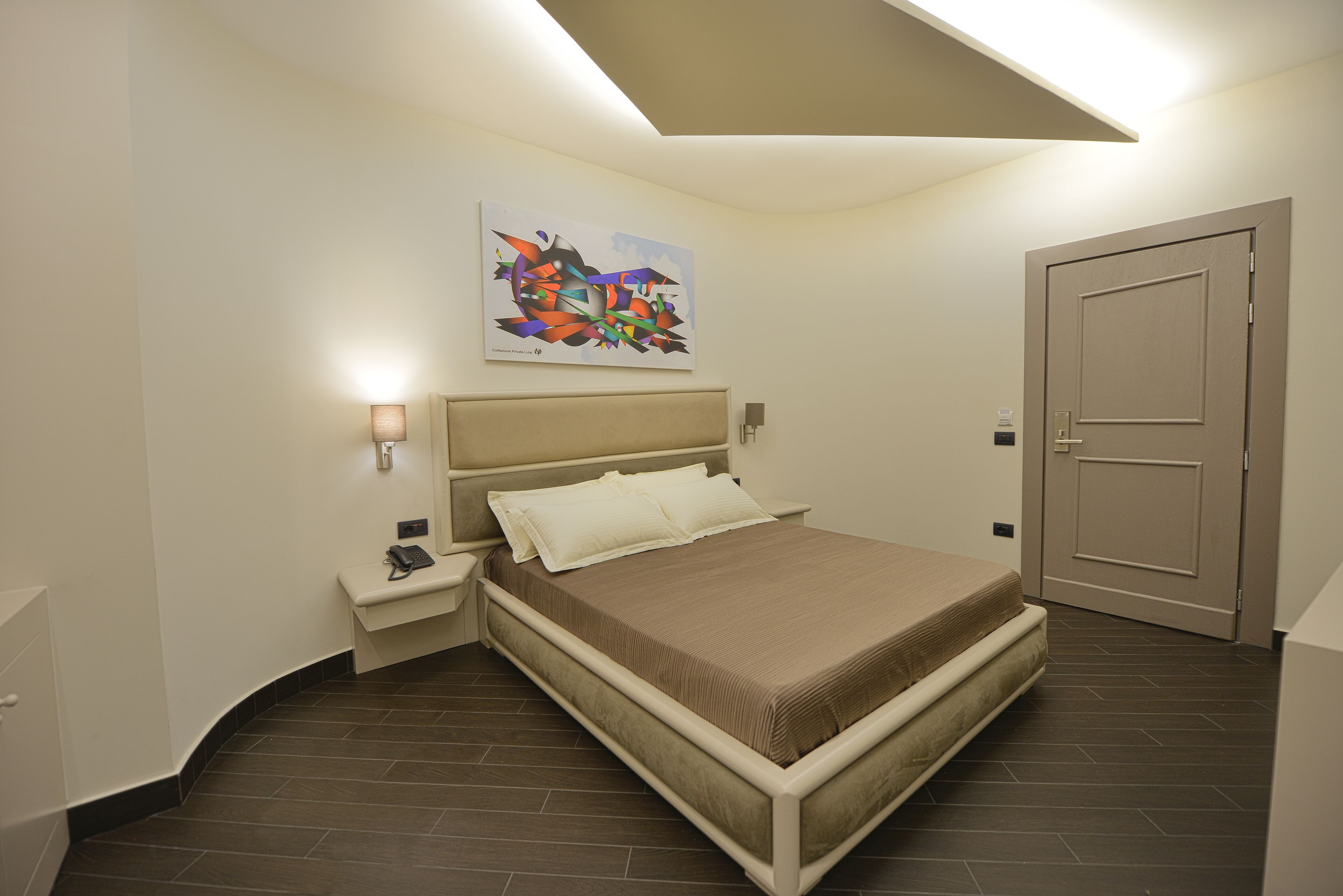 Un dormitorio moderno con cama, mesitas de noche, una puerta y una lámpara en el techo.
