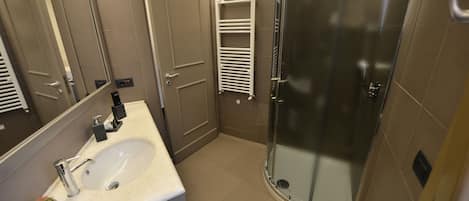 Een moderne badkamer met een wastafel, spiegel, douche en handdoekhouder.