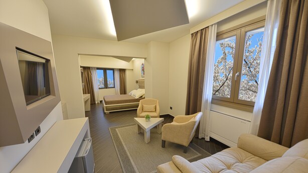 Una sala de estar moderna con un sofá, un sillón y una pequeña mesa. Hay un televisor montado en la pared y una ventana con cortinas.