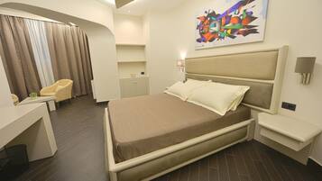 A modern hotel room with a bed, a desk, a chair, and a painting on the wall.