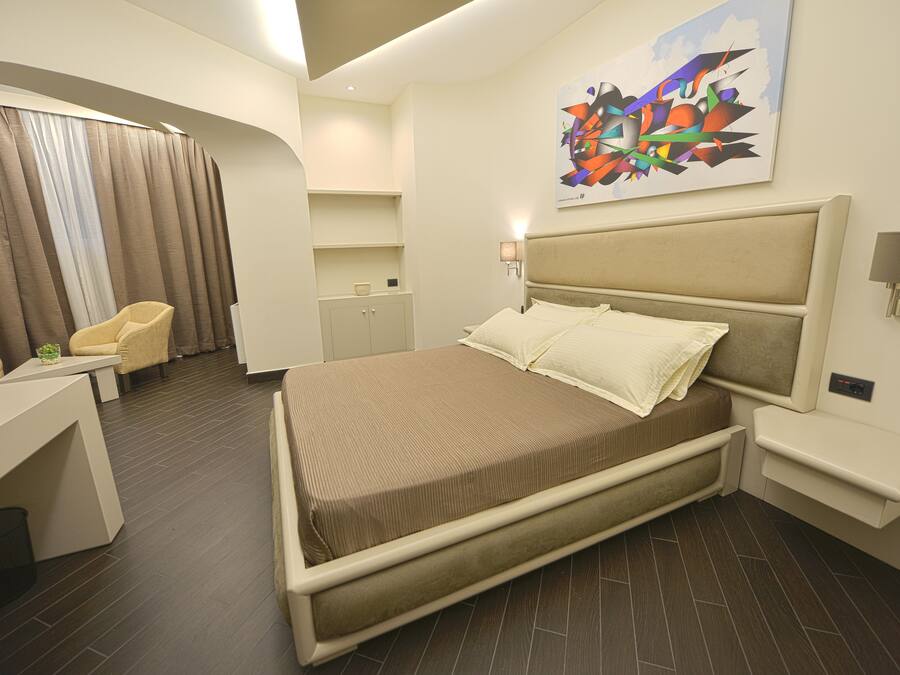A modern hotel room with a bed, a desk, a chair, and a painting on the wall.