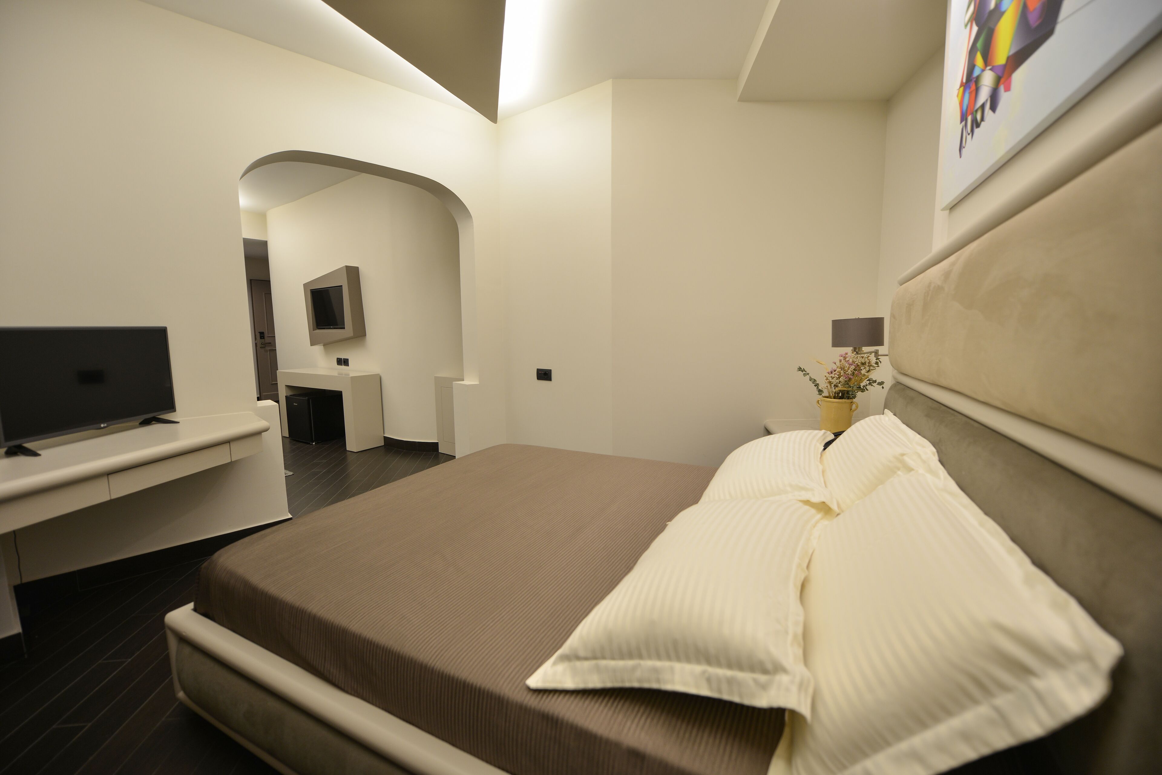 A modern hotel room with a large bed, a flat-screen TV, a desk, and a small seating area.