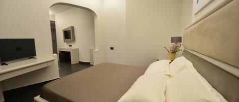 A modern hotel room with a large bed, a flat-screen TV, a desk, and a small seating area.