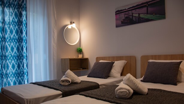 A hotel room with two beds, a bedside table, a wall-mounted light, a small plant, and a painting on the wall. - B&M House (Kissamos)